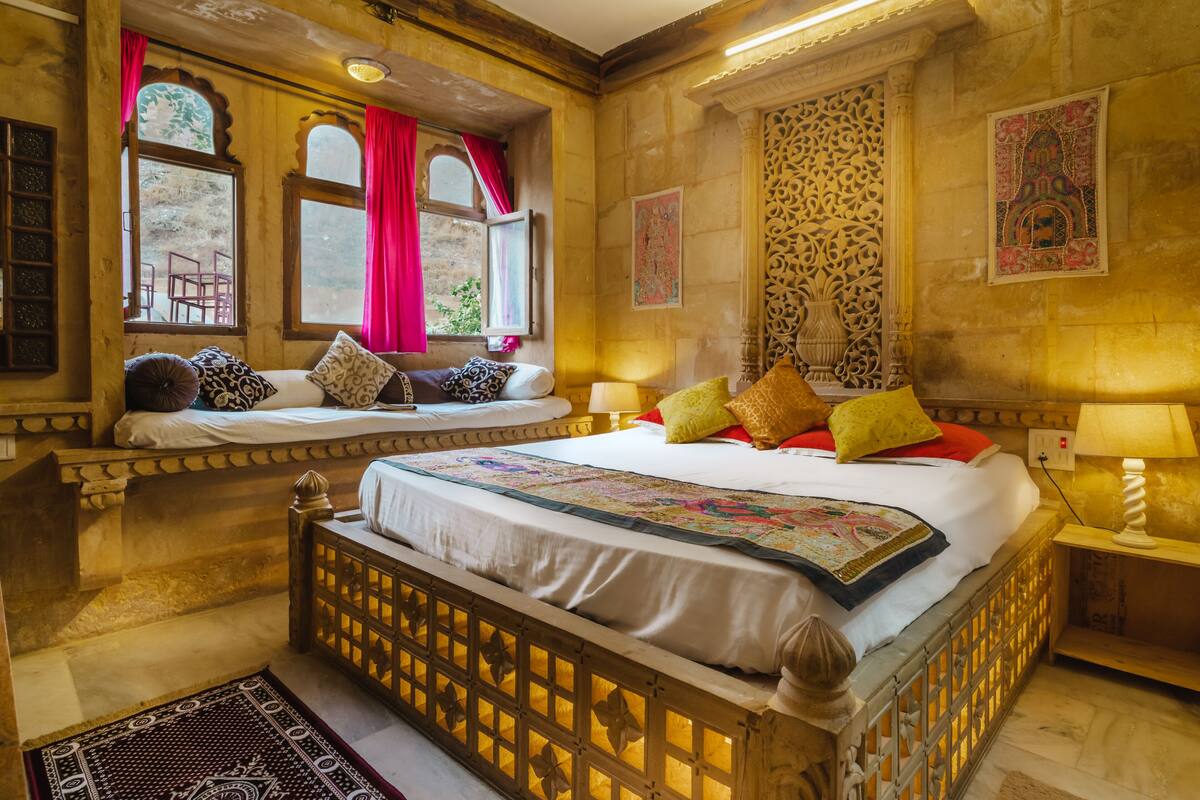 Quarto tradicional com uma cama grande, um assento junto à janela e um detalhe decorativo na parede.