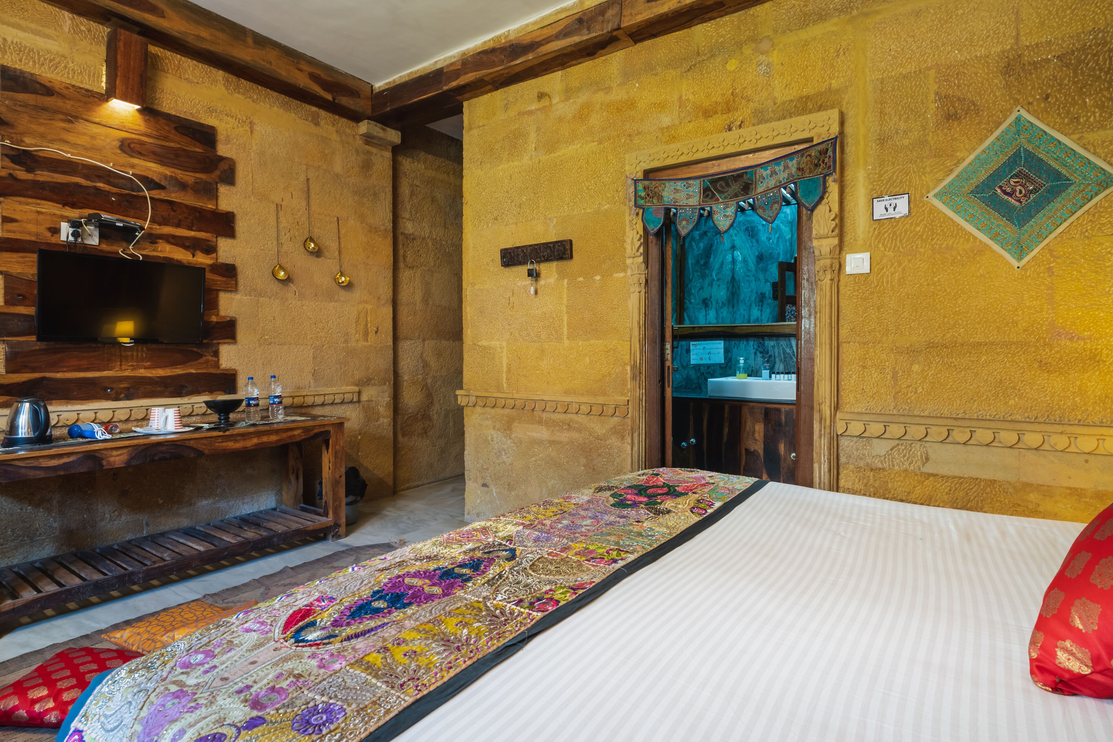 A room with a bed, a wooden bench, a television, and a decorative wall.