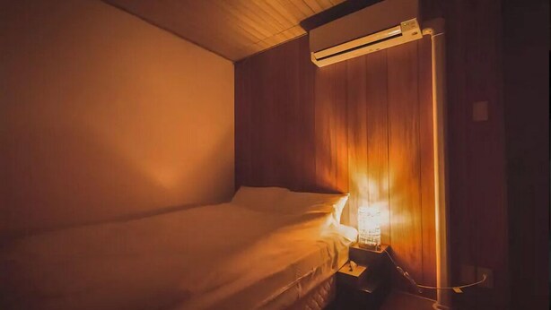 A single bed in a room with wooden walls and a ceiling fan. - Leisurely House (Kyoto)