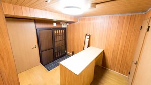 A wooden interior with a reception desk, a sliding door, and a ceiling light fixture. - Leisurely House (Kyoto)