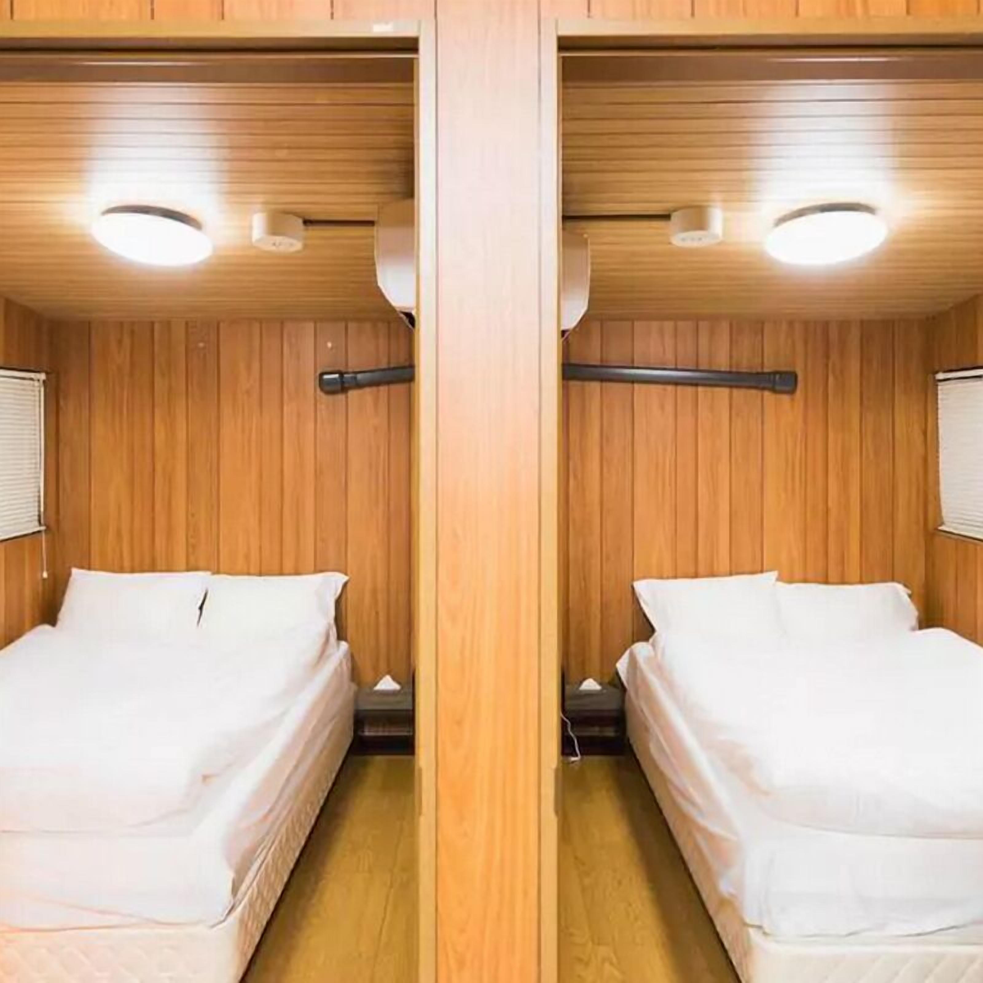 A mirrored room with wooden walls and ceiling, two beds with white bedding, and a small bedside table with a lamp.