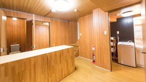 A wooden interior with a reception desk, a staircase, and a kitchen area. - Leisurely House (Kyoto)