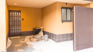 A hallway with a wooden door, a small fire pit, and a tiled floor. - Leisurely House (Kyoto)