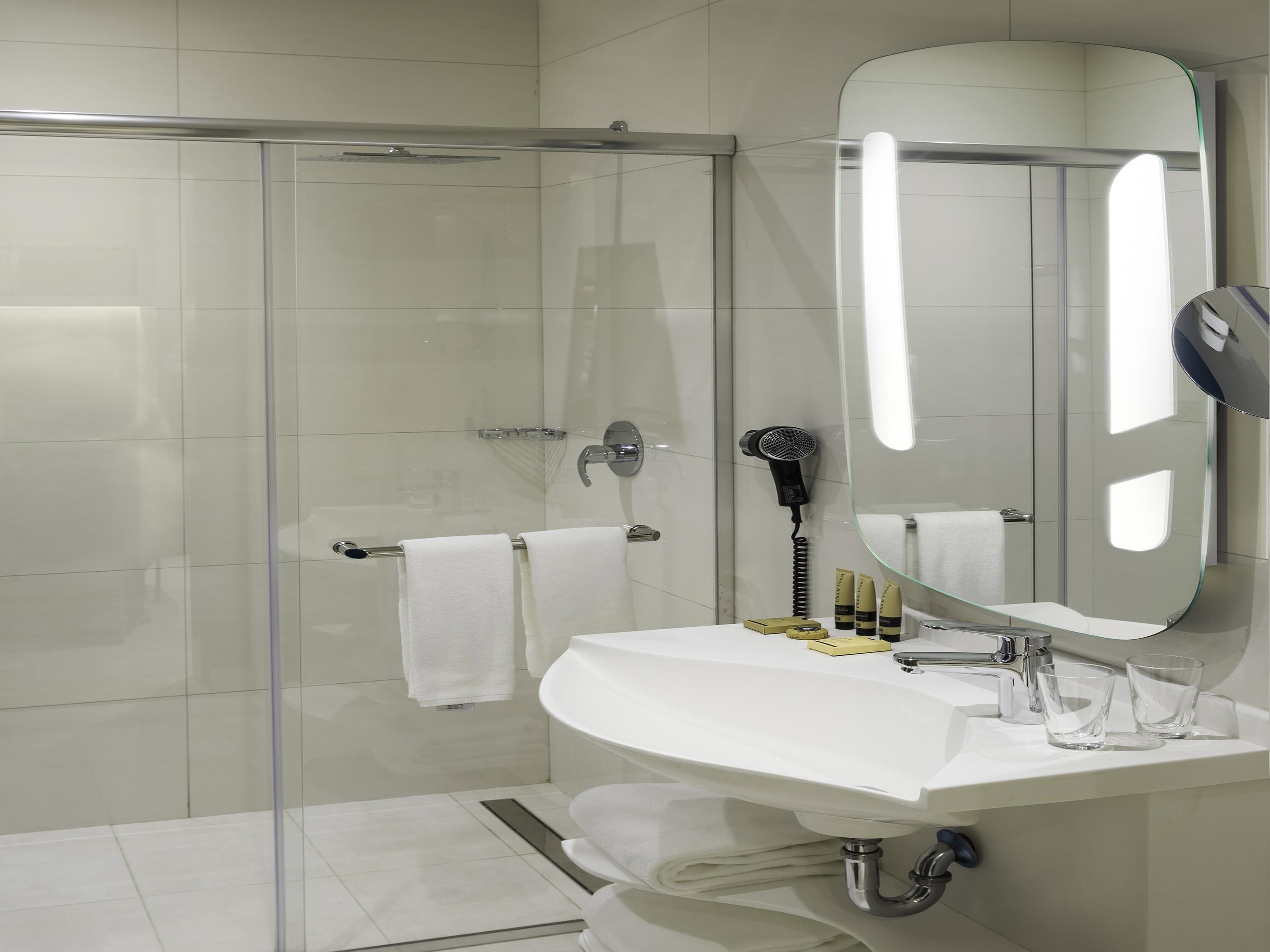 A modern bathroom with a glass shower enclosure, a white sink with a mirror, and a towel rack.