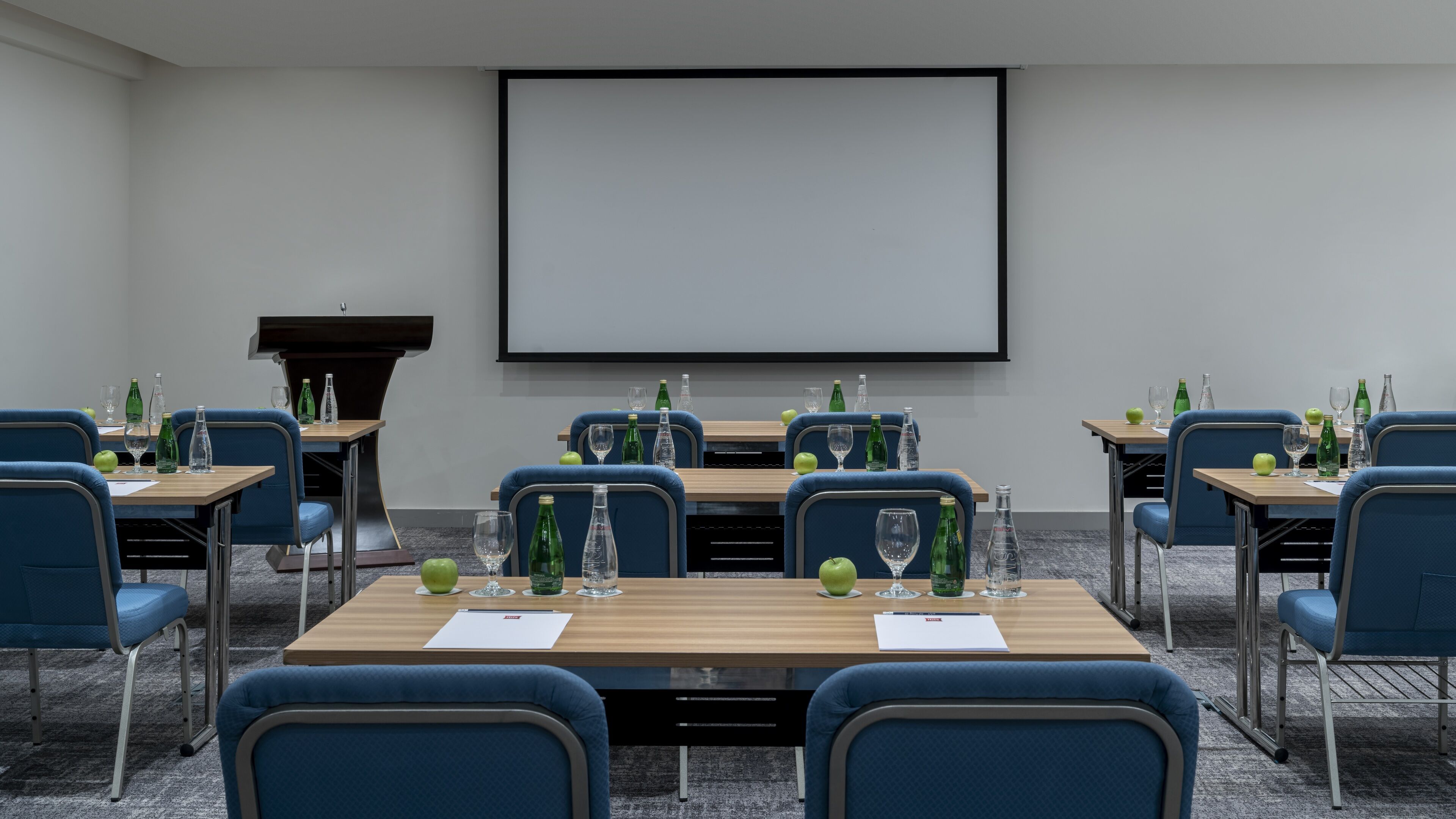 Uma sala de conferências com mesas, cadeiras e um projetor.