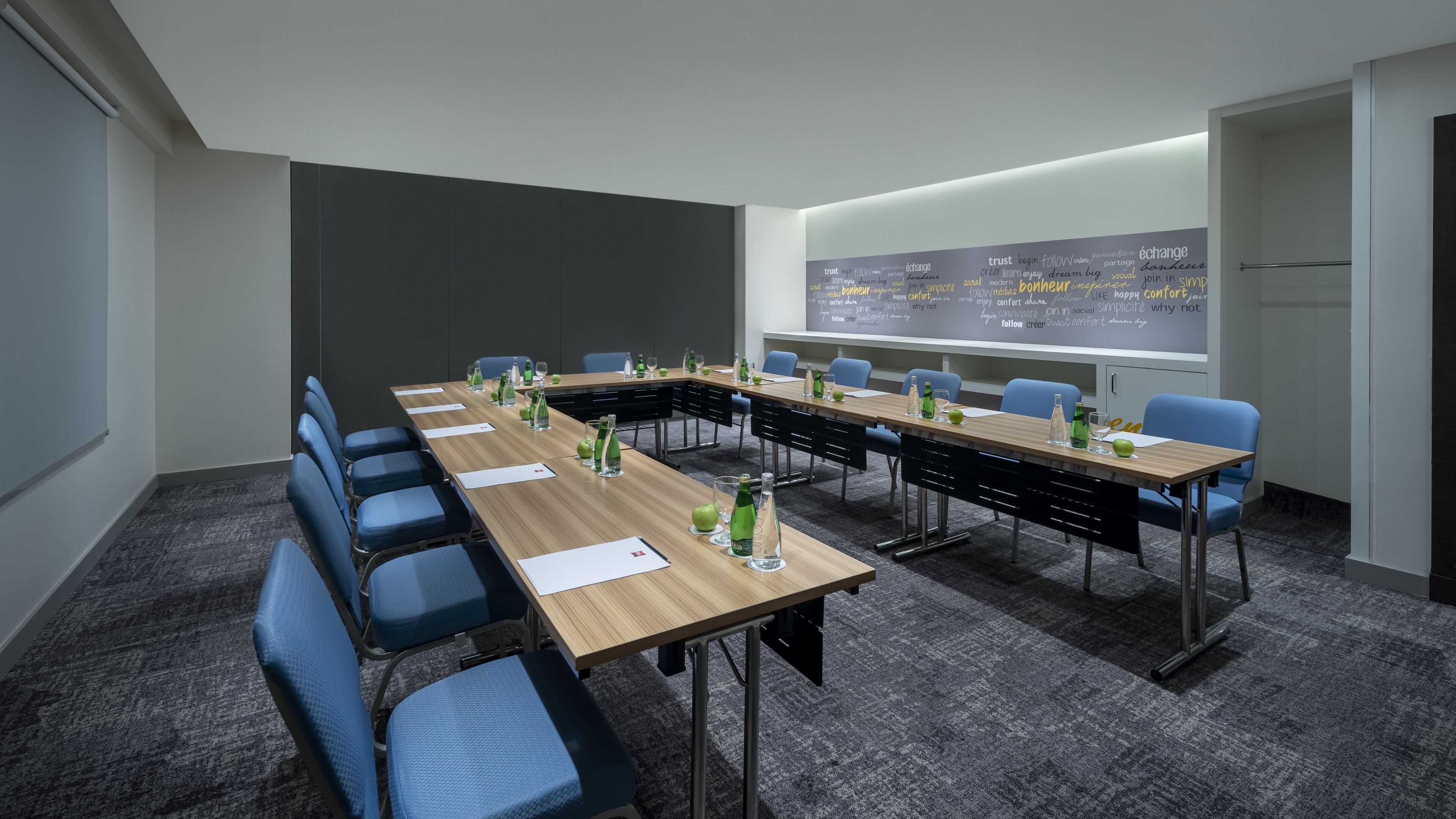 A conference room with a long table, blue chairs, and a whiteboard with motivational words.