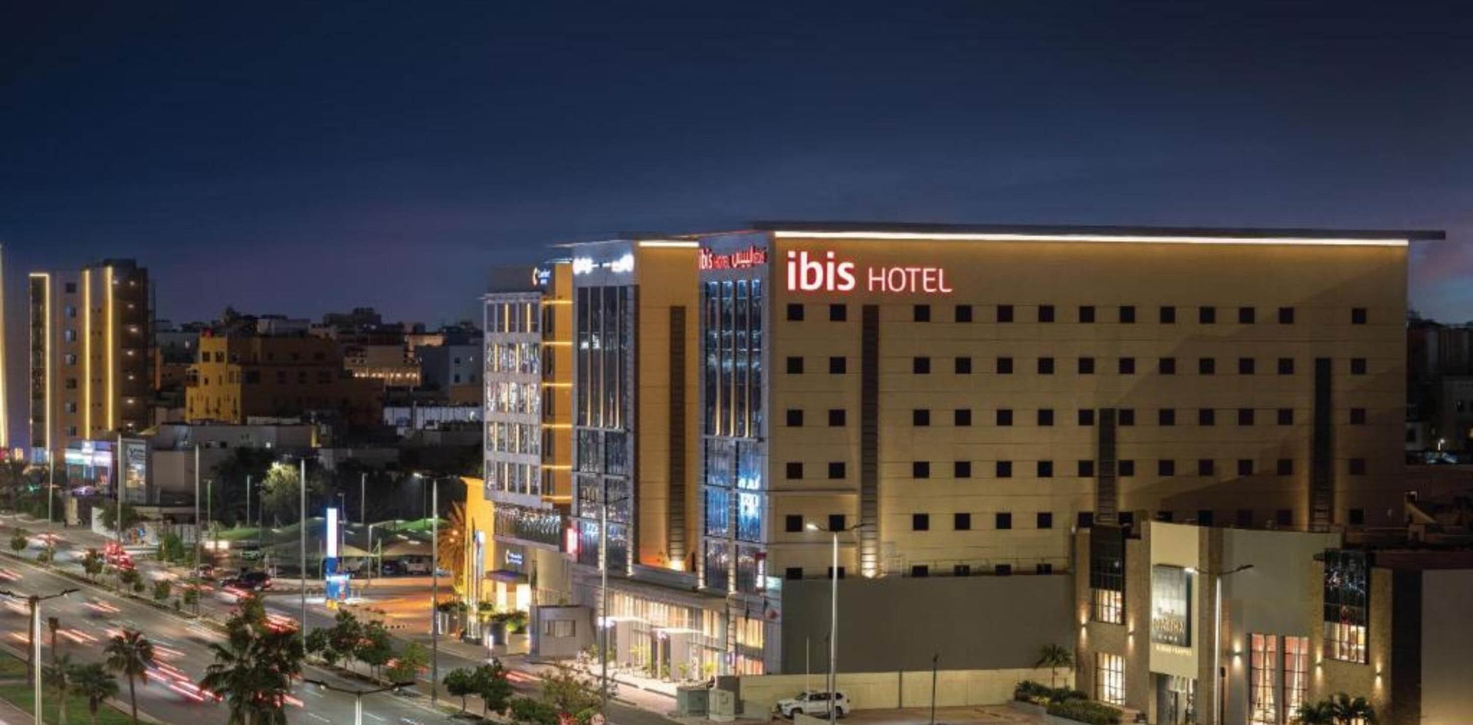 Un hôtel moderne, reconnaissable à son grand panneau « ibis HOTEL », qui se distingue par sa façade plate et ses nombreuses fenêtres.