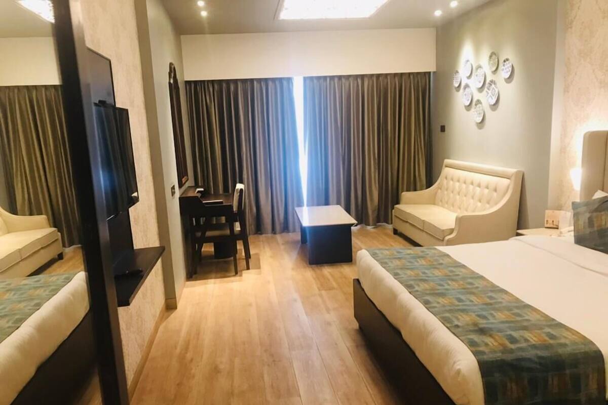 Habitación de hotel con dos camas, un sofá, una mesita y un televisor.