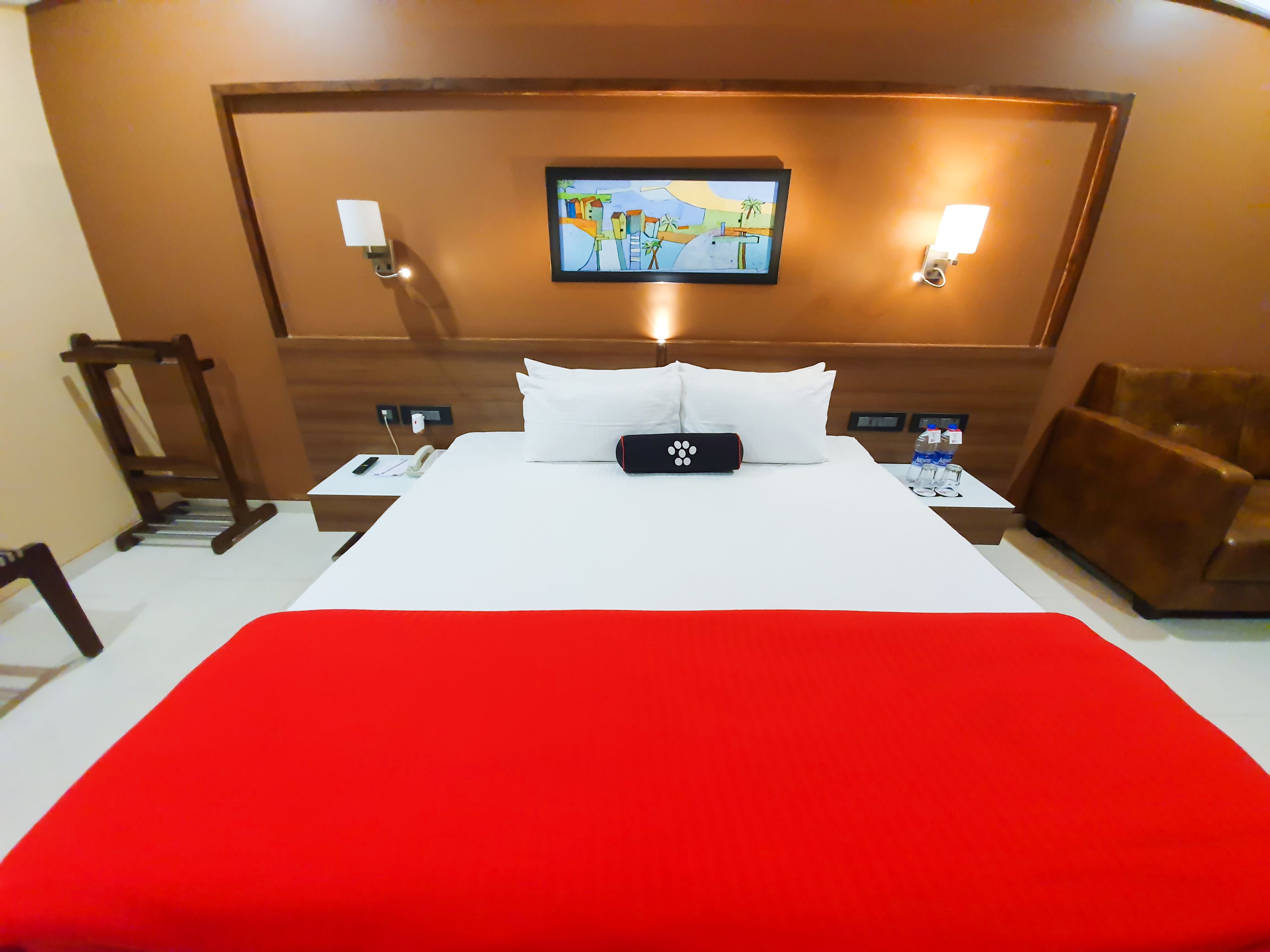 A hotel room with a large bed, a bedside table with a phone and a lamp, a wall-mounted TV, and a brown leather armchair.