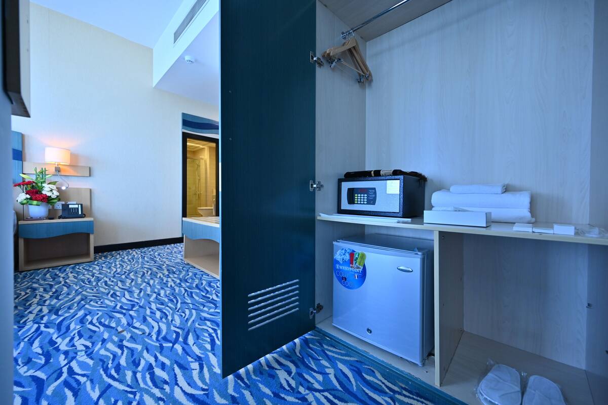 A hotel room with a patterned carpet, a minibar, a small refrigerator, and a towel rack.