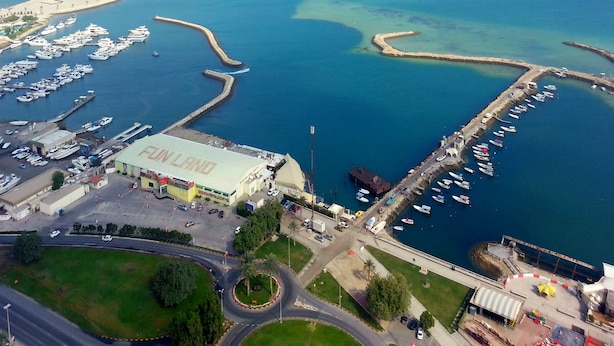 An aerial view of a marina with boats docked, a roundabout, and a large building labeled "FINLAND". - Harbour Suites Hotel from Holiday Gulf Hotel (Manama)
