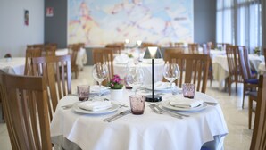 A dining area with round tables set for a meal, featuring white tablecloths, wine glasses, and cutlery.