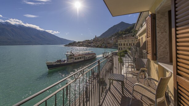 A balcony with a view of a lake, a boat, and mountains in the background.