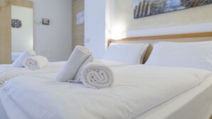 A hotel room with a neatly made bed, a painting on the wall, and a door in the background.