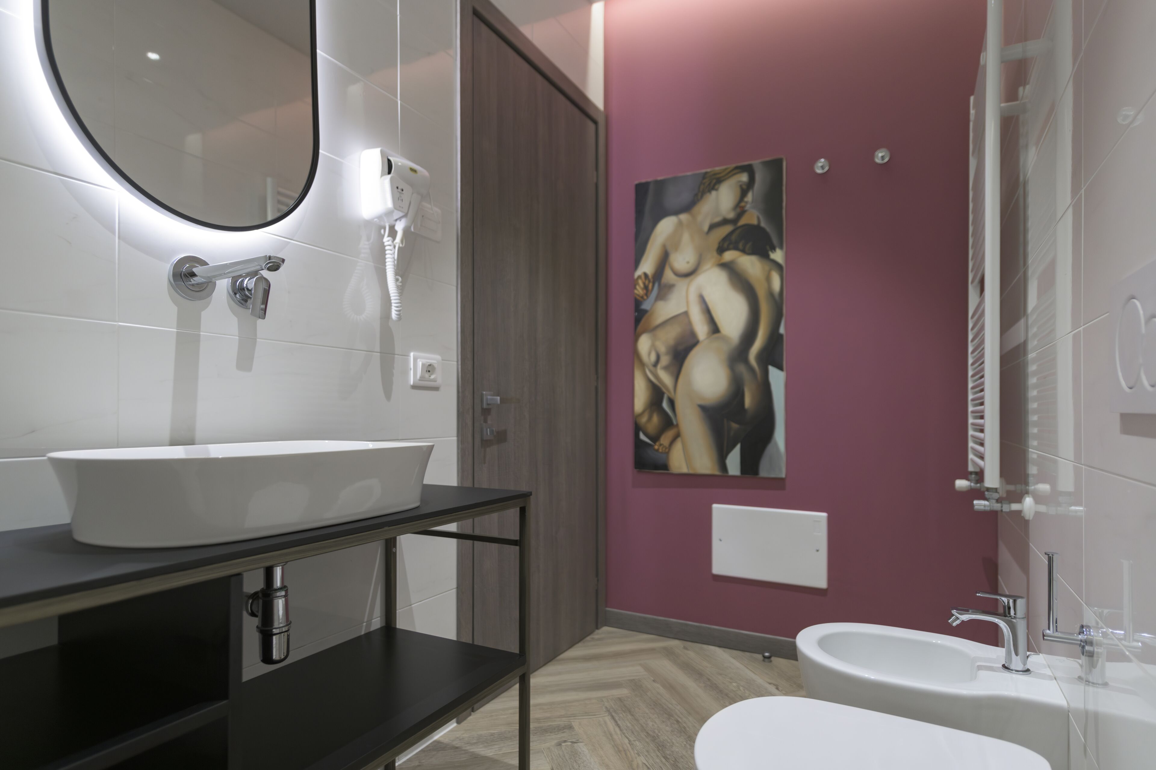 A modern bathroom with a large oval sink, a mirror, a handheld hair dryer, and a painting on the wall.