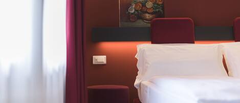 Una habitación de hotel con una cama, una silla roja, una mesita y un cuadro en la pared.