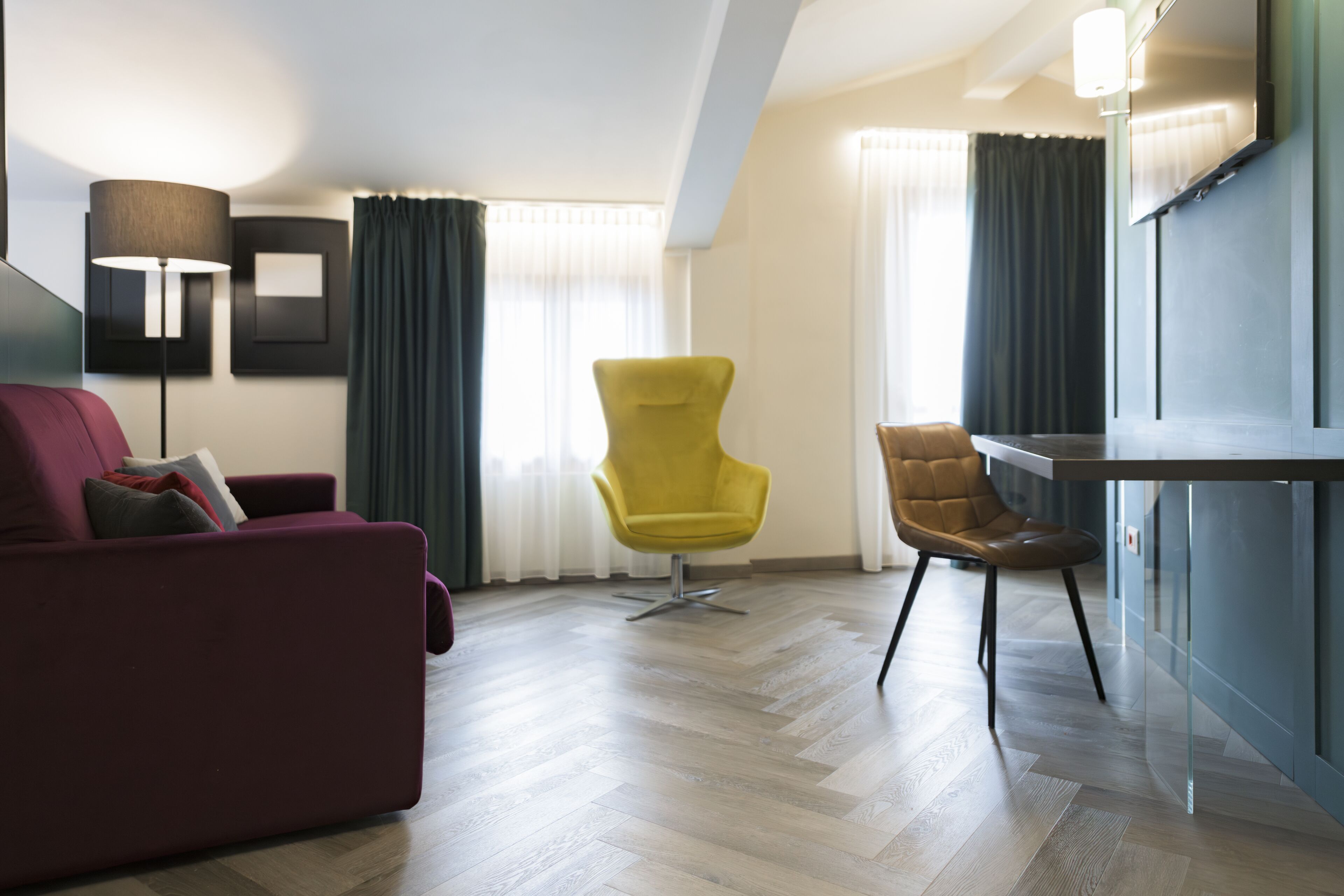 Una sala moderna con un sofá rojo, un sillón amarillo y una silla marrón. Hay un televisor montado en la pared y una lámpara de pie.