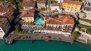 An aerial view of a coastal hotel with a swimming pool, outdoor seating, and a waterfront promenade.