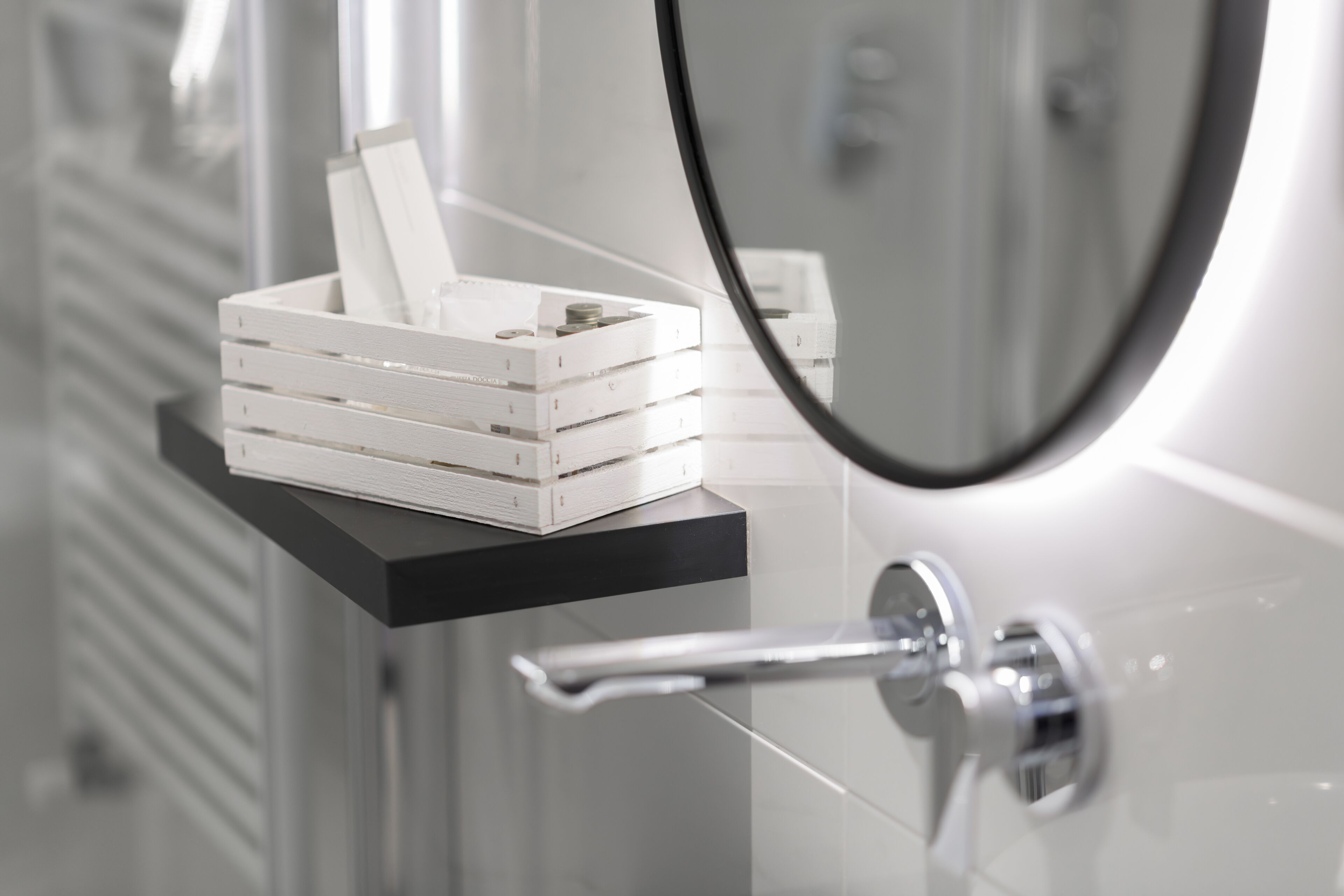 A bathroom with a white shelf holding a white box and coins, a chrome faucet, and a mirror.