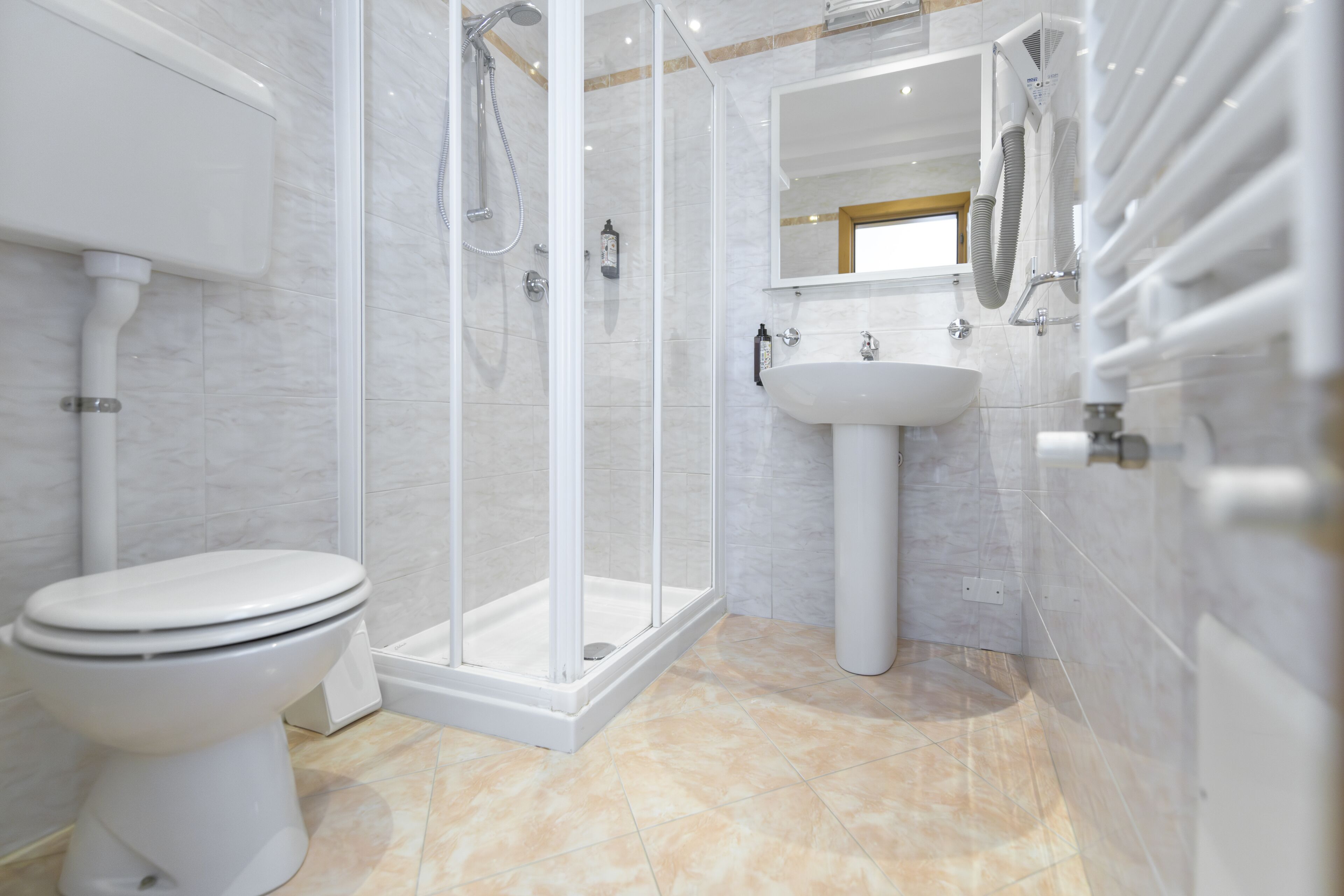 Een moderne badkamer met een toilet, een douche met glazen wanden en een wastafel op een zuil.
