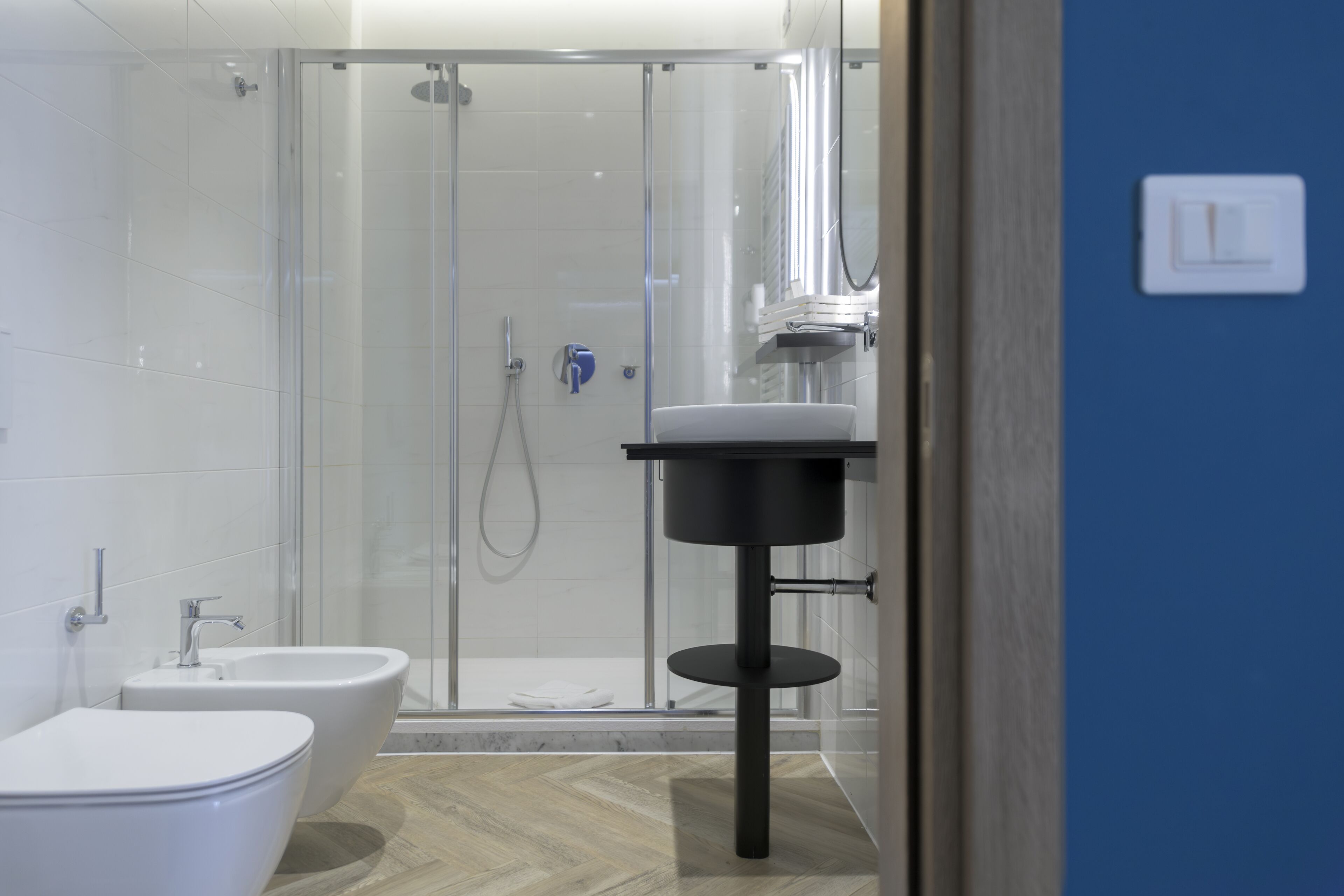 A modern bathroom with a glass-enclosed shower, a white sink, and a bidet.