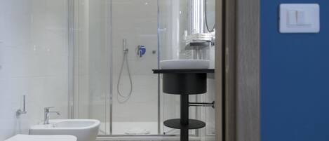 A modern bathroom with a glass-enclosed shower, a white sink, and a bidet.