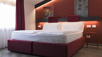 Una habitación de hotel moderna con una cama grande, cabecera tapizada en rojo y un cuadro en la pared.