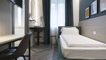 Une chambre d’hôtel équipée d’un lit, d’un bureau, d’une chaise, d’un miroir, d’un lavabo et d’une fenêtre avec des rideaux.