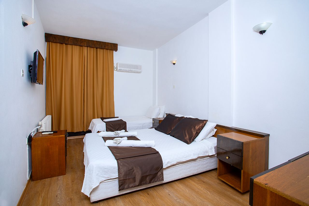 A hotel room with two beds, a wooden desk, a TV, and a window with curtains.