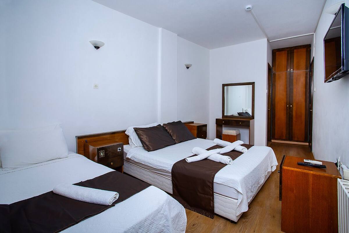 A hotel room with two beds, a wooden wardrobe, a mirror, and a television.