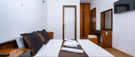 A hotel room with a bed, a TV, a wooden wardrobe, and a door.