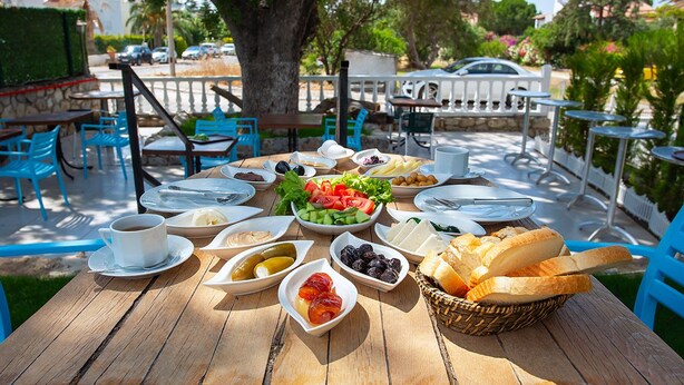 Un área de comedor al aire libre con una mesa de madera dispuesta con diversos alimentos y una taza de café.