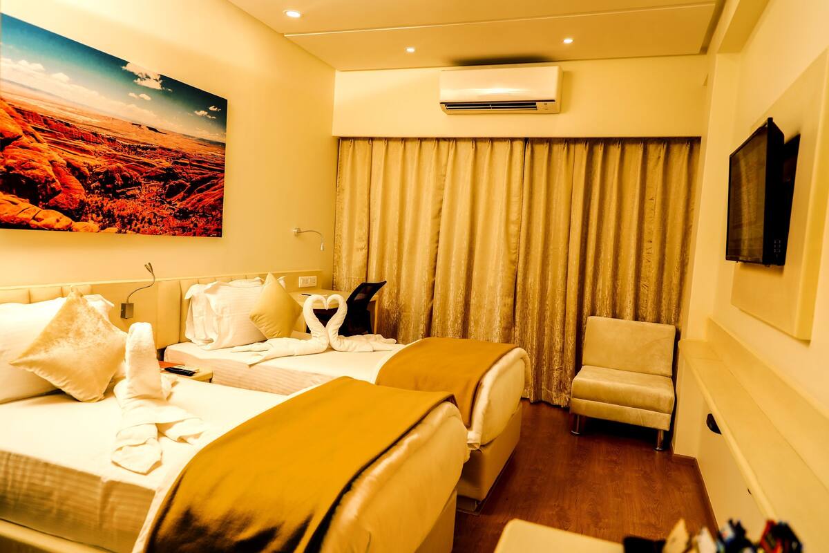 A hotel room with two beds, a chair, an air conditioning unit, a painting on the wall, and a curtain.