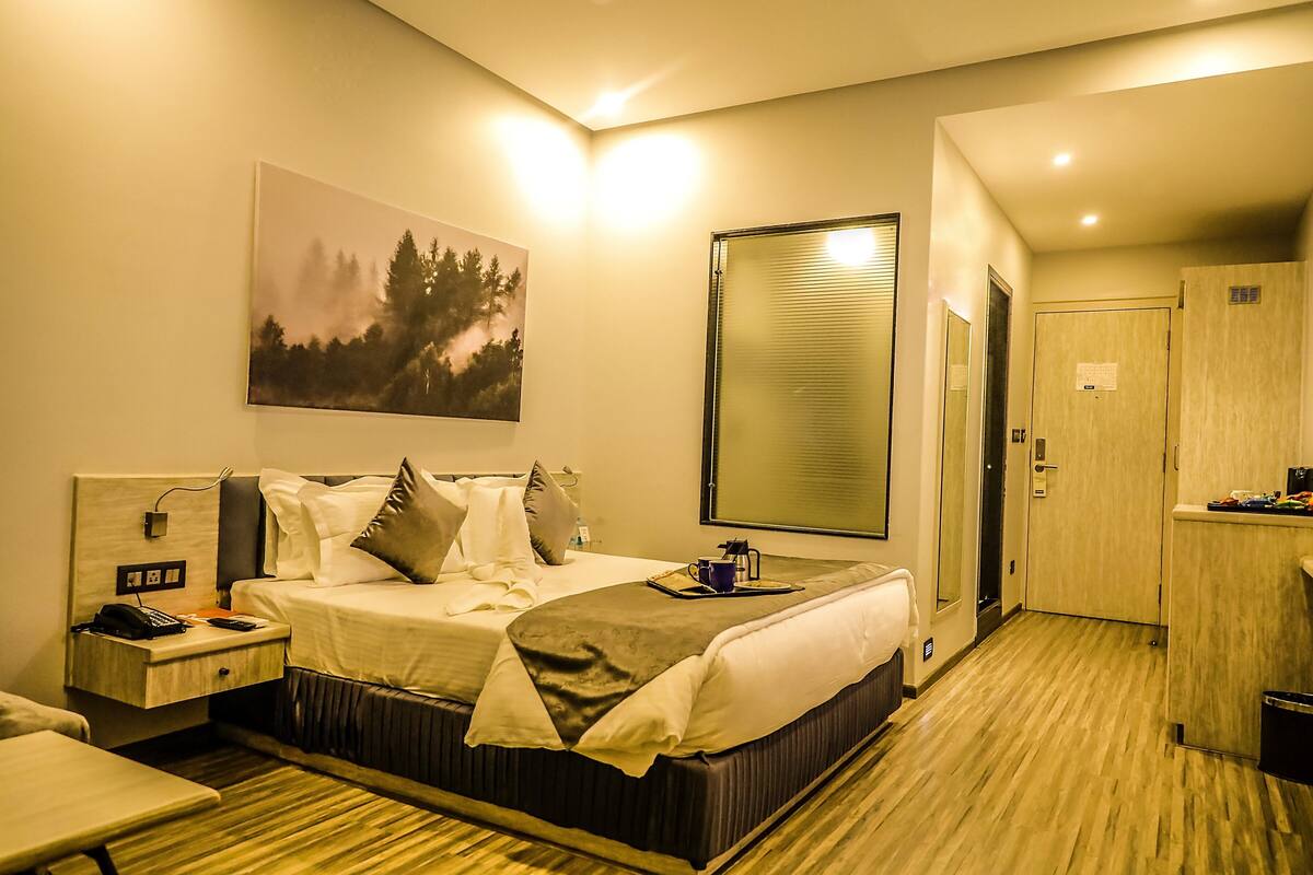 A hotel room with a bed, bedside table, and a painting on the wall.