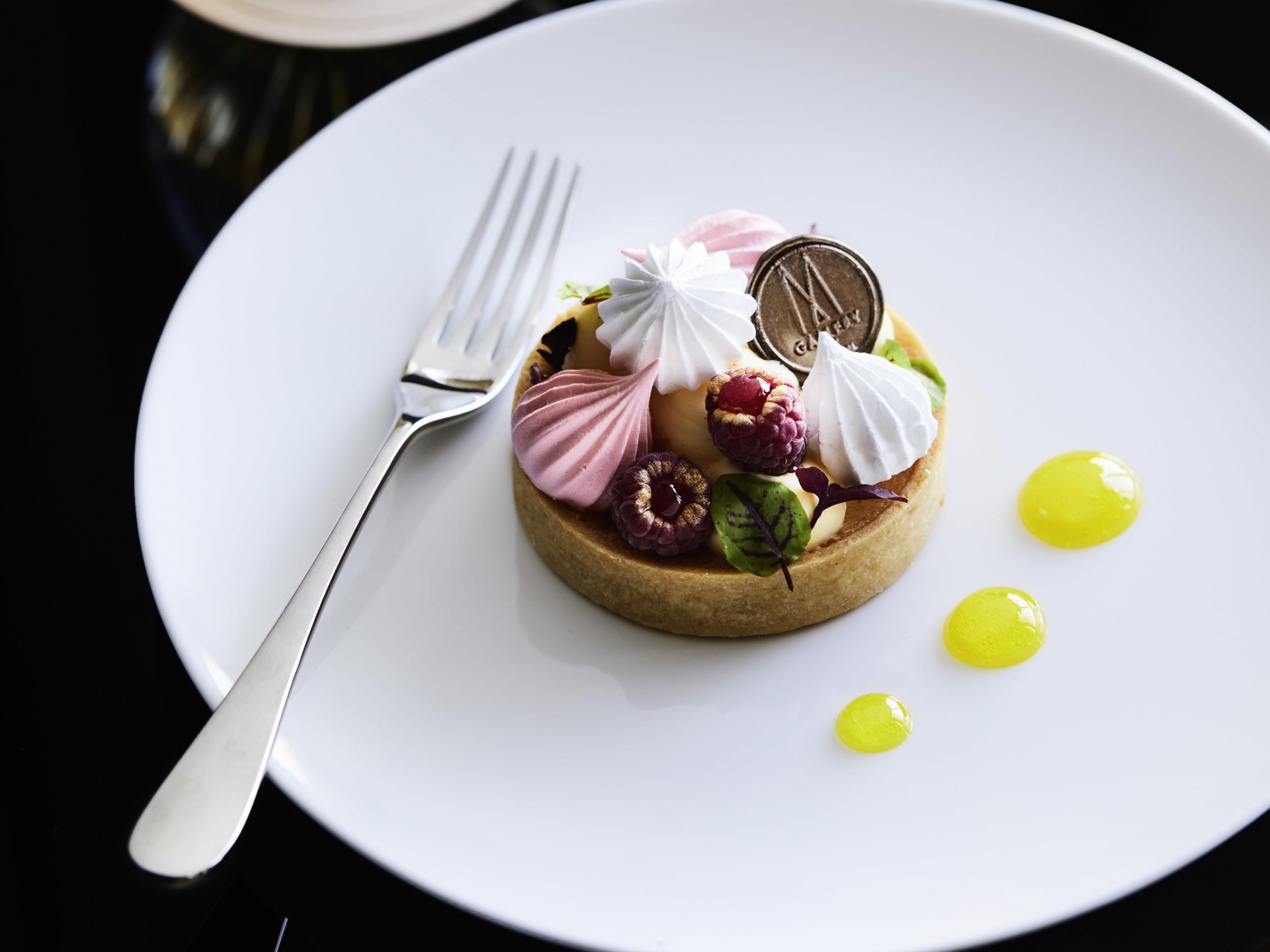 A dessert on a white plate with a fork, featuring meringue, raspberries, and a chocolate coin.
