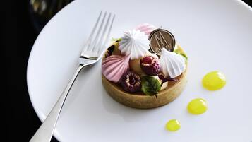 A dessert on a white plate with a fork, featuring meringue, raspberries, and a chocolate coin.