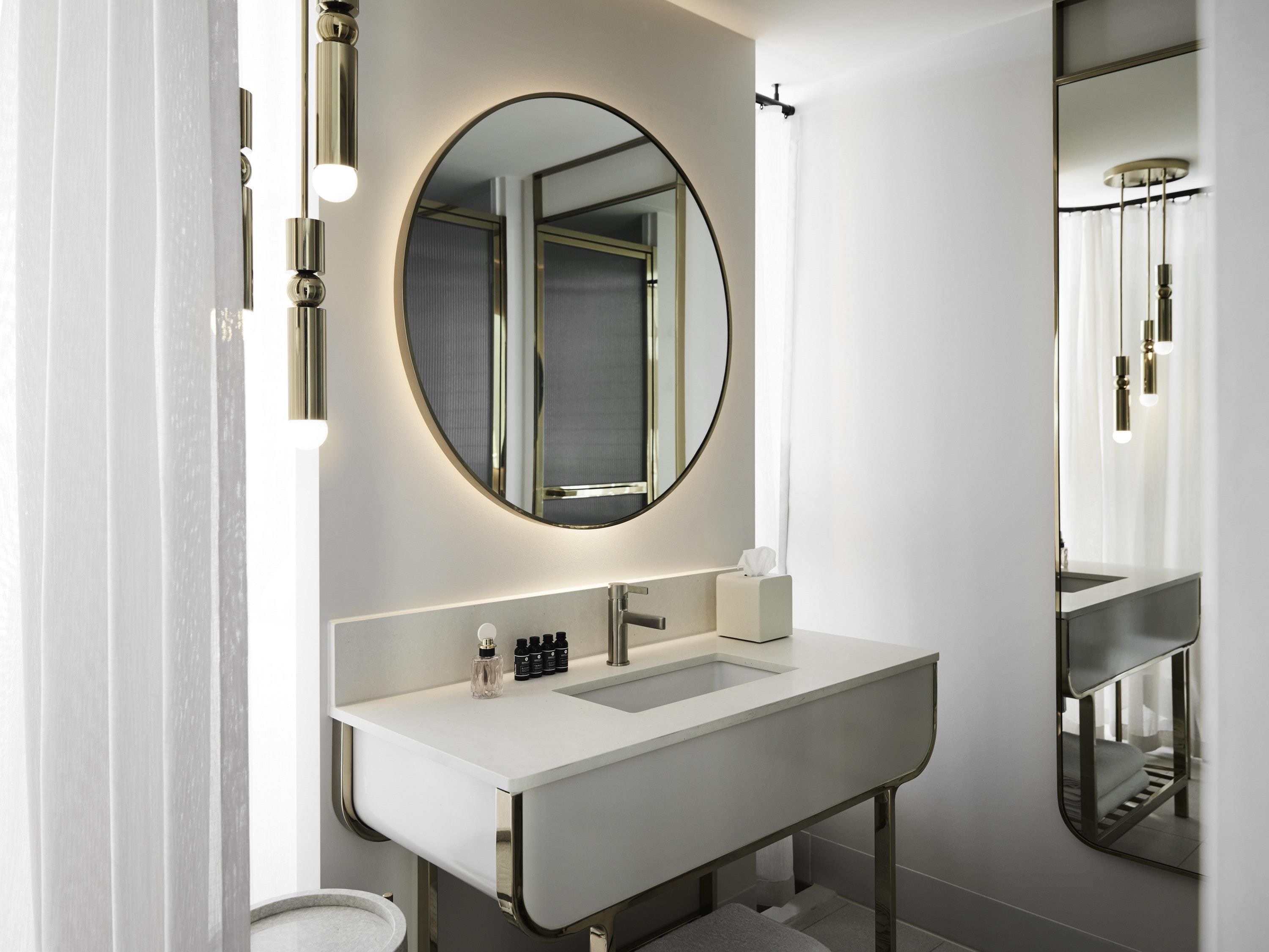 Un baño moderno con un tocador blanco, un espejo redondo y un espejo grande sobre el lavamanos.