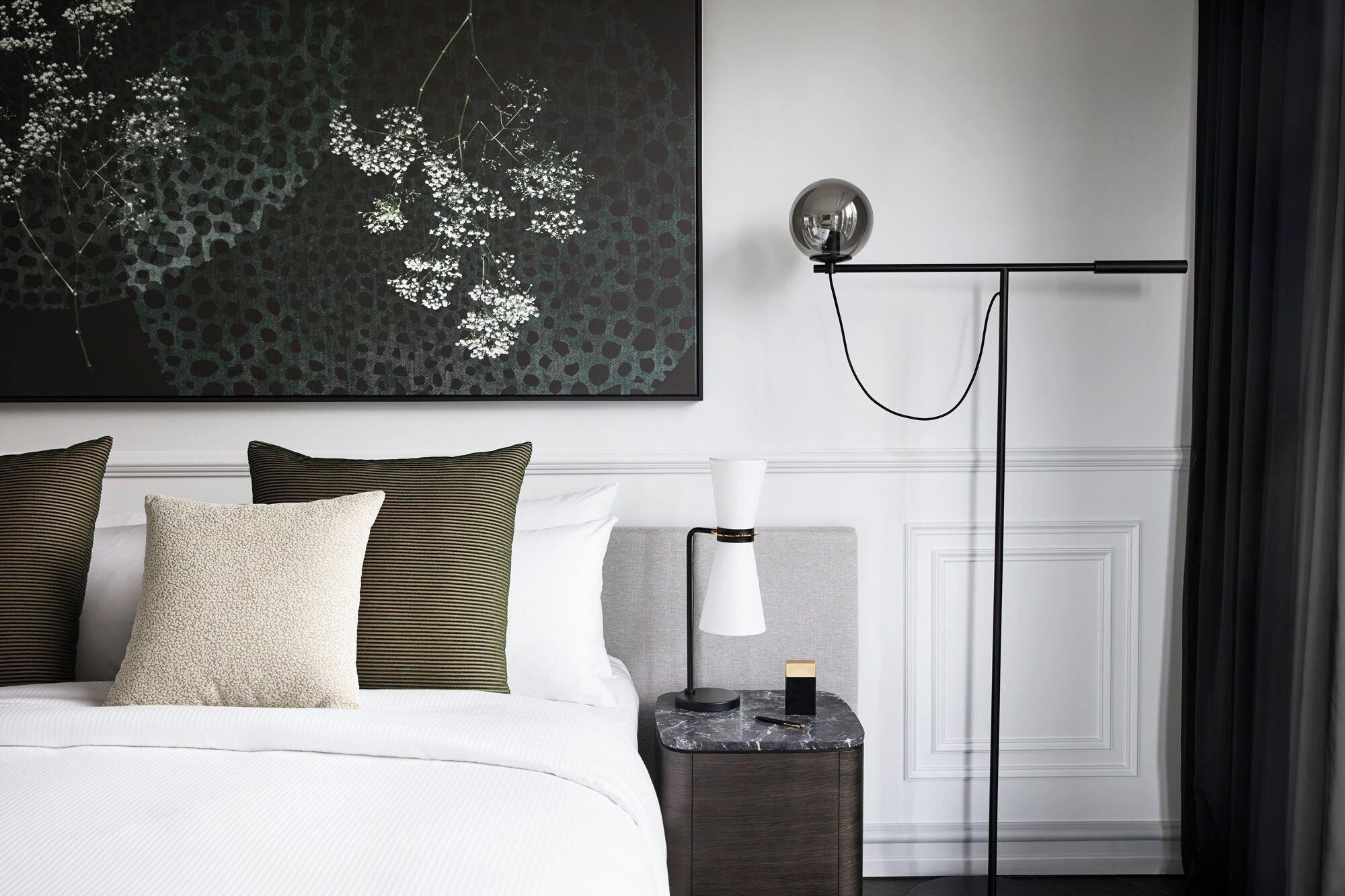 A modern bedroom with a bed, pillows, a nightstand, a lamp, and a wall-mounted light fixture.