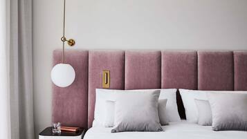 A neatly made bed with white bedding, a pink upholstered headboard, and a bedside table with a glass and a book.