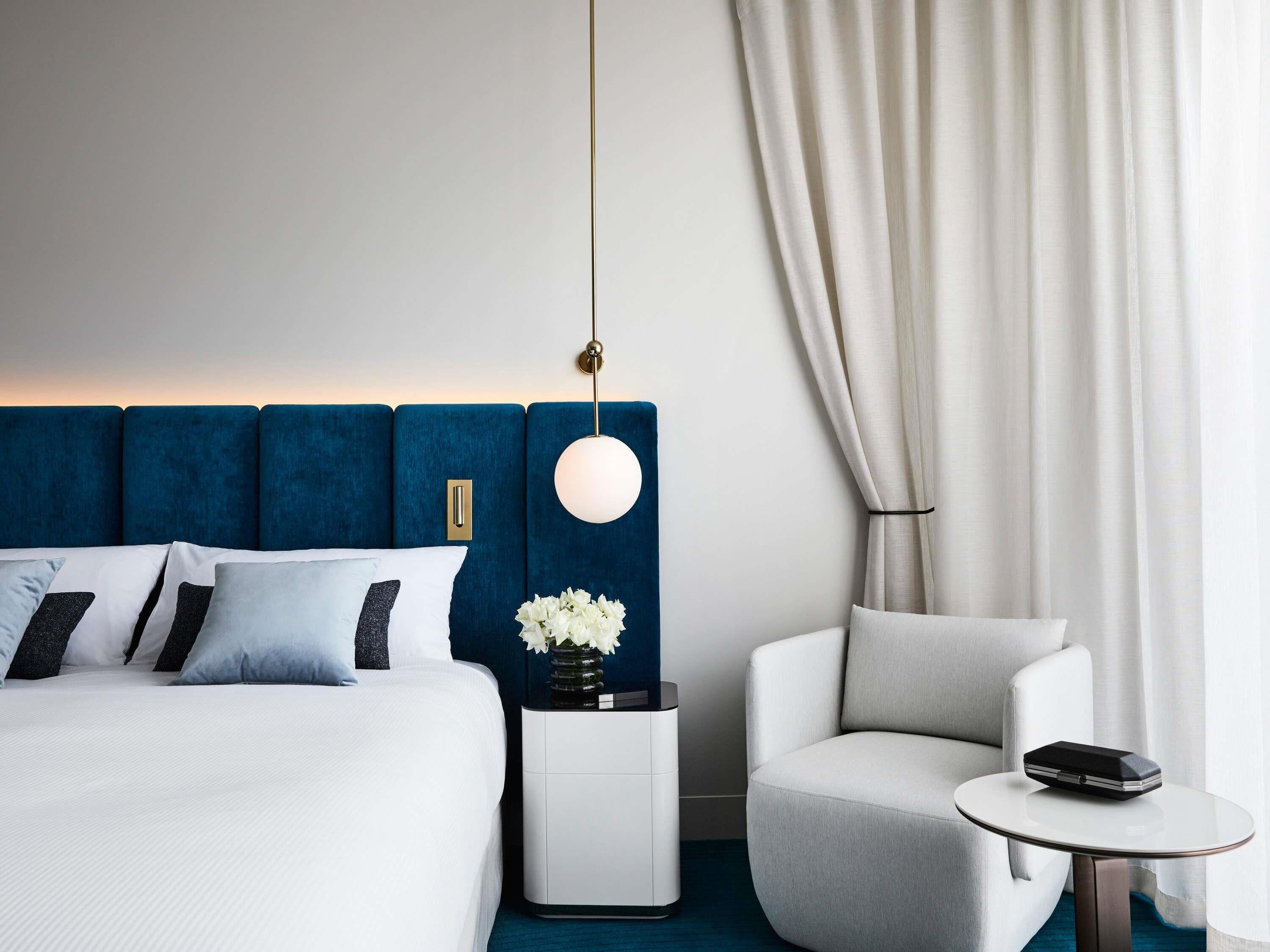 A modern hotel room with a large bed, a bedside table with a vase of flowers, a round table with a phone, and a chair.