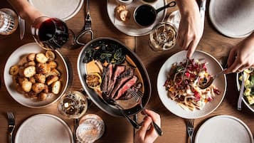 A dining table with various dishes, including roasted potatoes, a steak, and a salad, along with multiple glasses of wine.