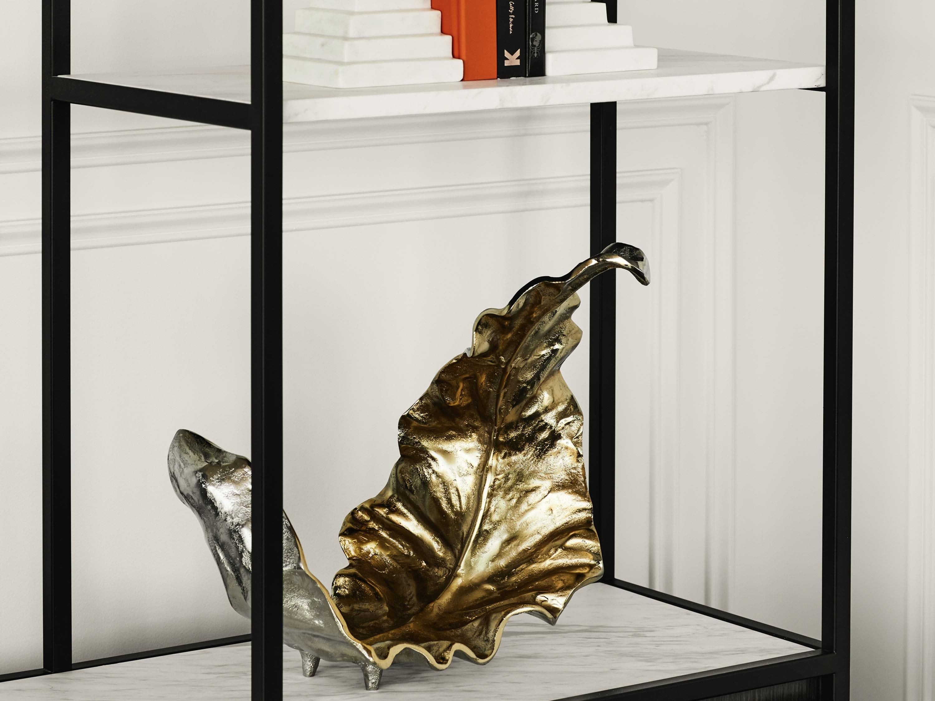 A metallic leaf sculpture on a white marble pedestal in a black-framed display cabinet.