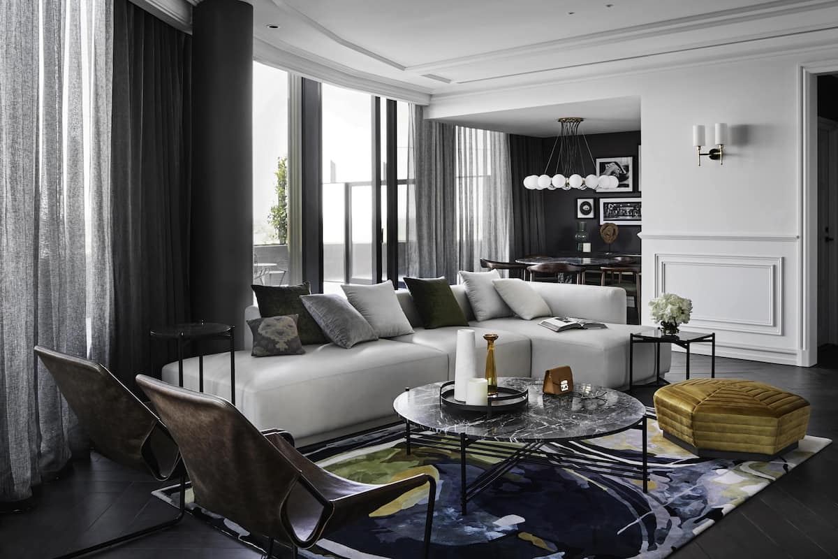 A modern living room with a sofa, chairs, a coffee table, and a dining area in the background.