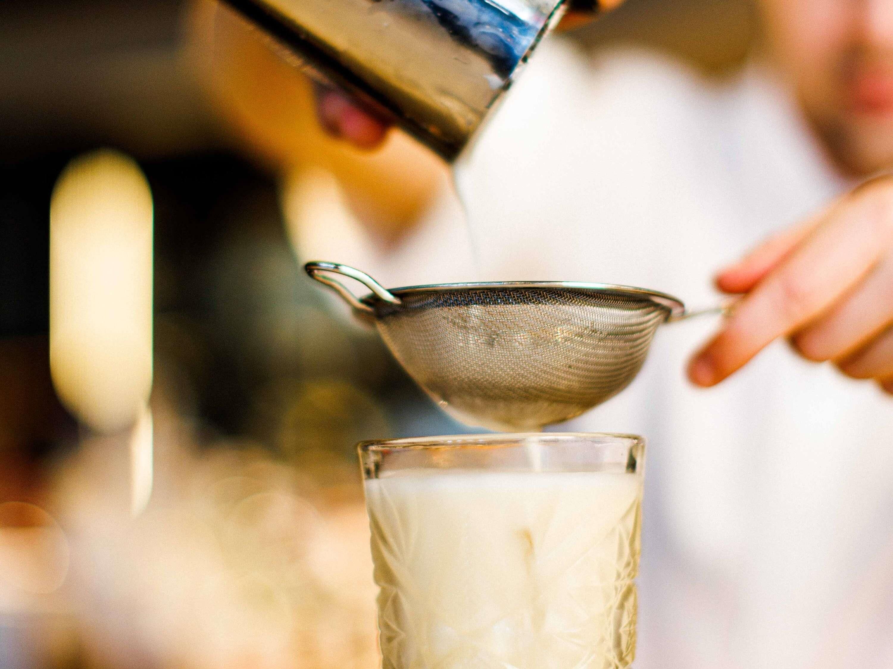 A person pouring milk into a glass using a strainer.