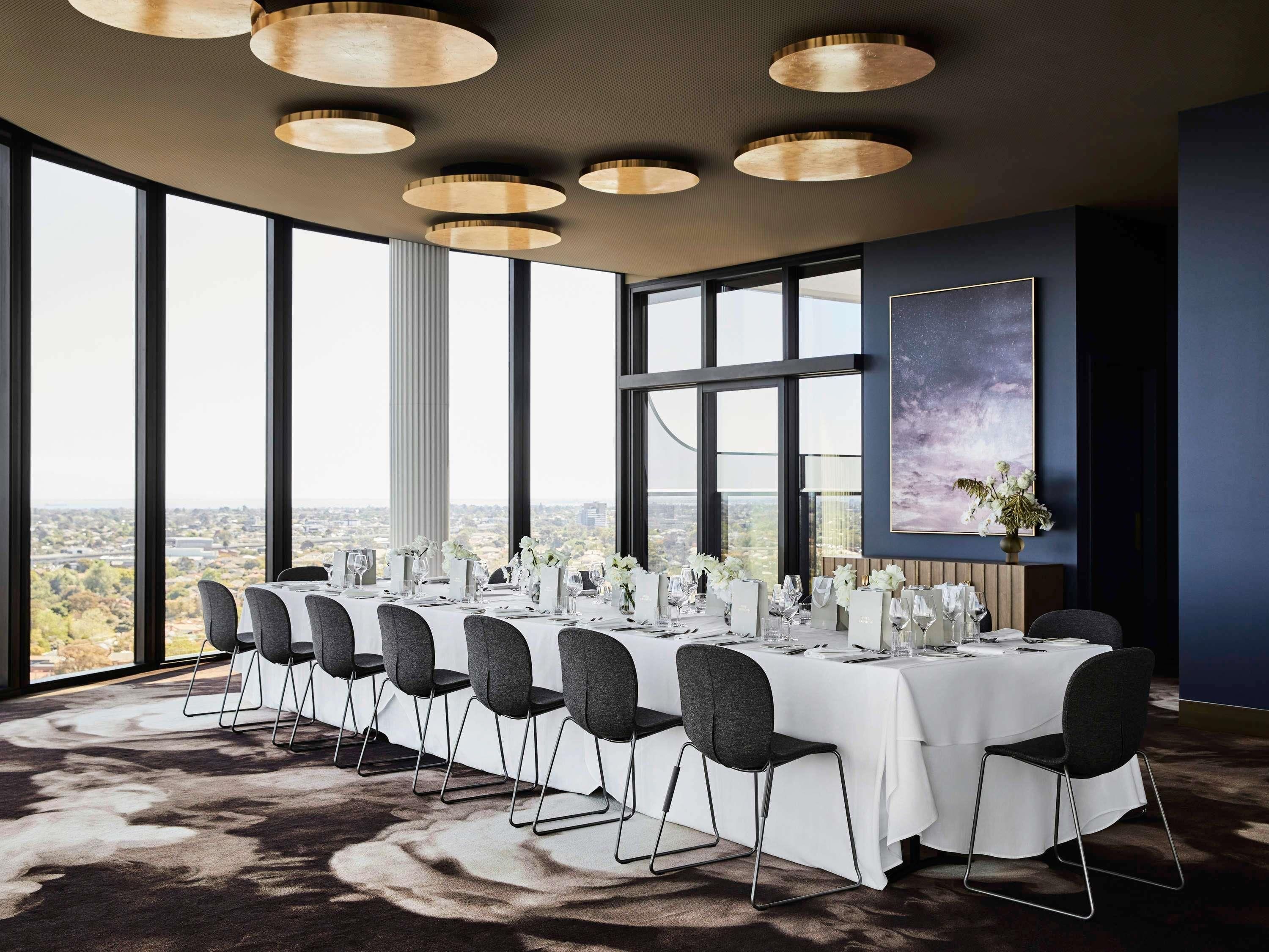 Un salón de conferencias con una larga mesa, varias sillas y ventanas amplias que ofrecen vistas a la ciudad.