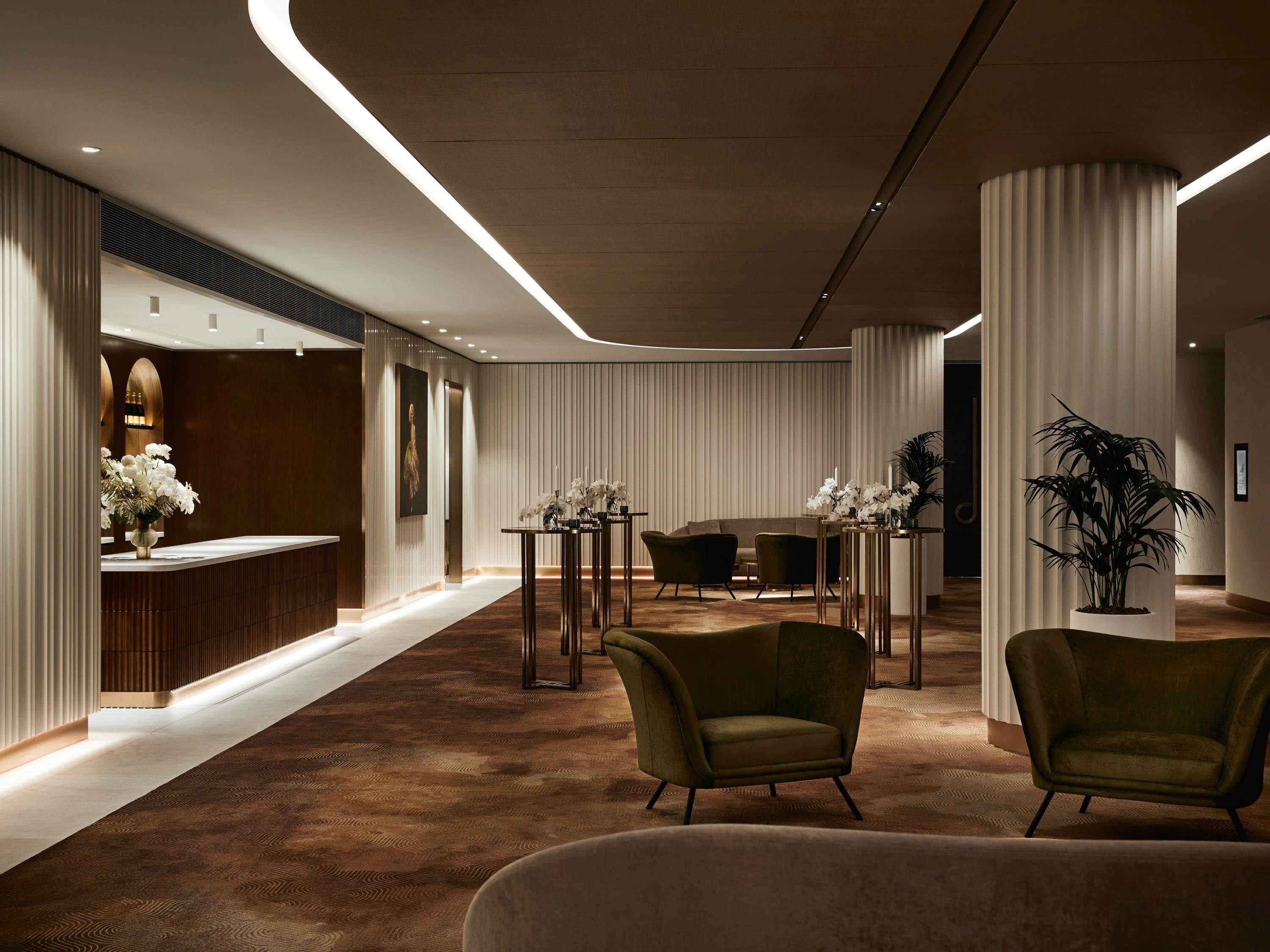 Un hall de hotel con mostrador de recepción, zona de estar y plantas decorativas.