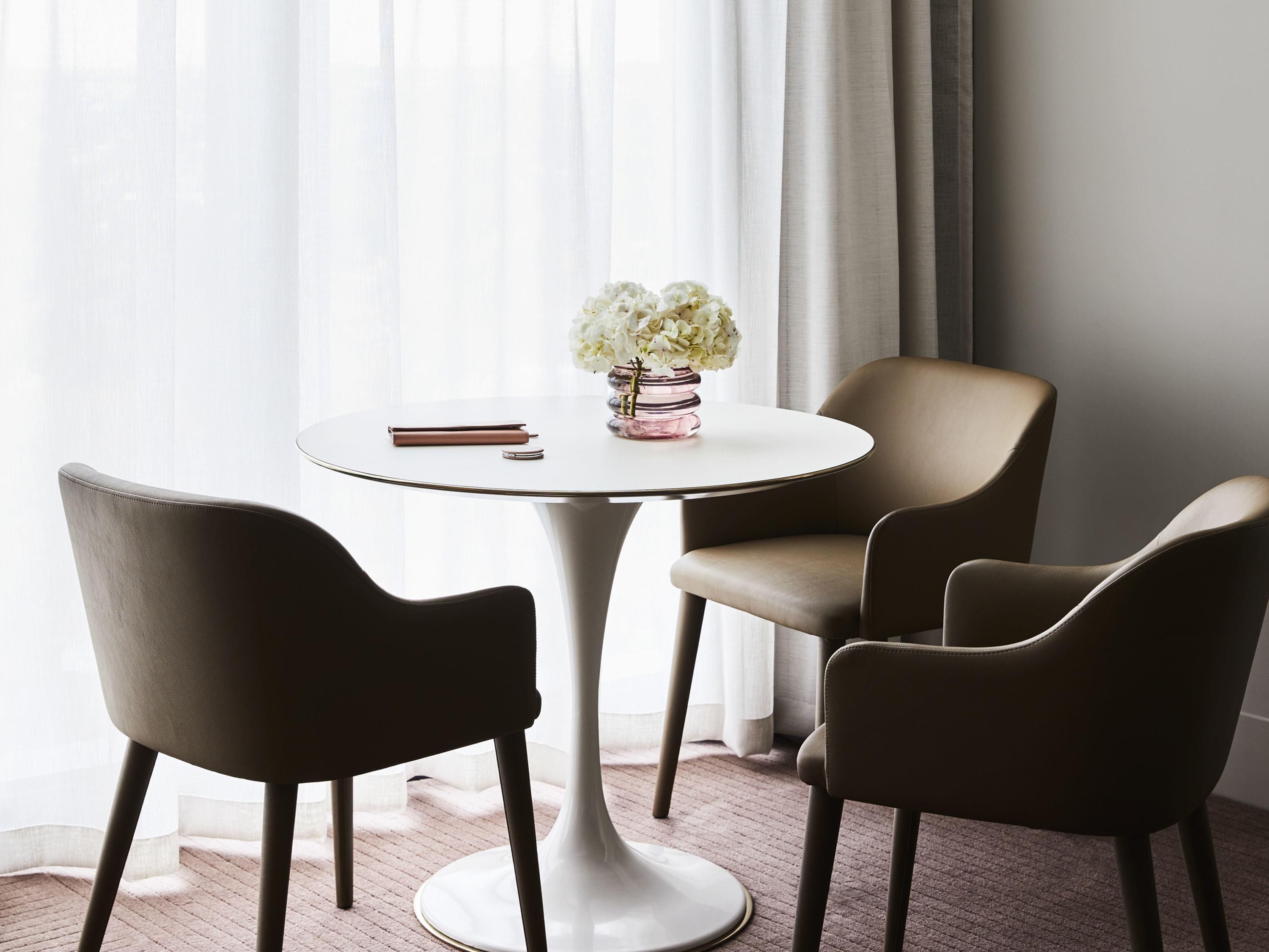 Une table ronde ornée d’un vase de fleurs blanches, deux chaises et un livre posé sur la table.