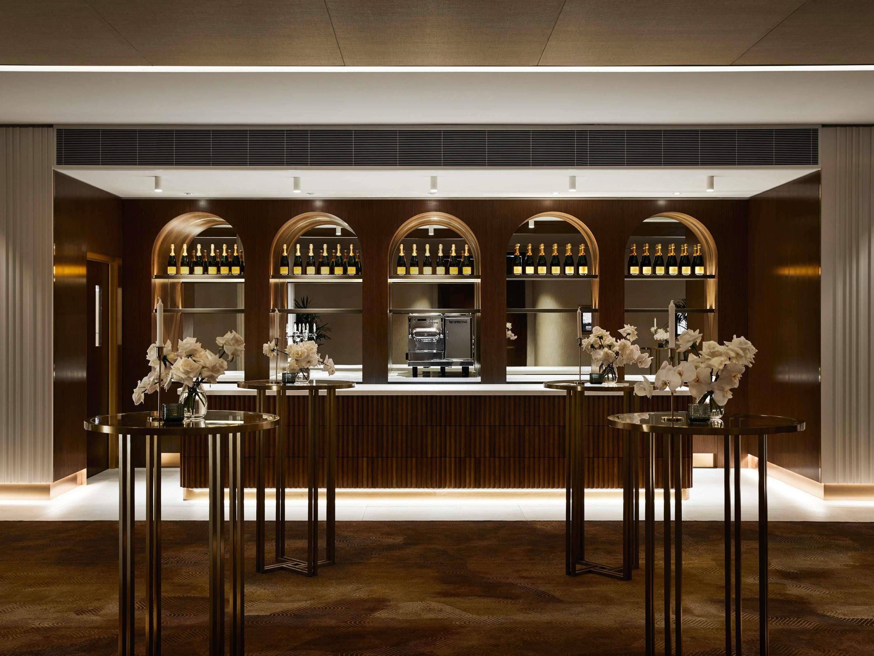 A bar area with a counter, multiple shelves of bottles, and tables with vases of flowers.