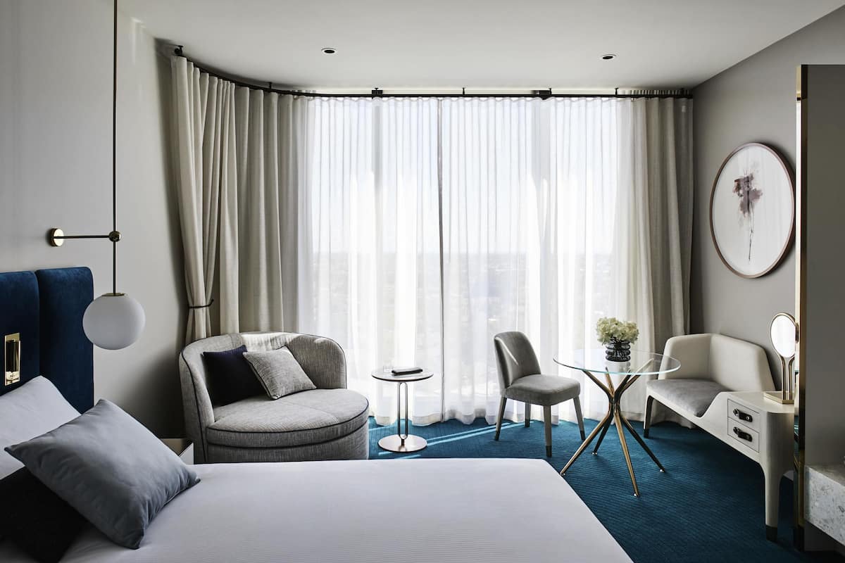 A modern hotel room with a large bed, a sofa, a small round table, and a chair.
