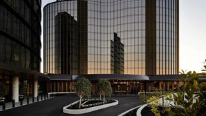 A modern building with a curved glass facade, surrounded by a landscaped area with trees and a paved walkway. - Hotel Chadstone Melbourne MGallery Collection (Chadstone)